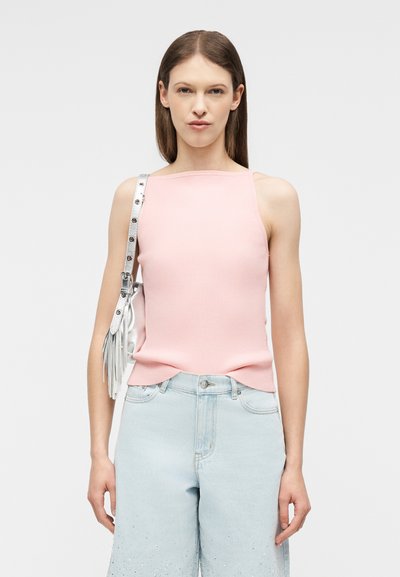 Γυναίκα με ίσια καστανά μαλλιά φορά ροζ αμάνικη μπλούζα, ανοιχτόχρωμα γαλάζια τζιν ψηλής μέσης με διακοσμητικά στοιχεία και ασημένια τσάντα ώμου με φούντες.