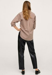 Chemise à rayures marron et blanche, coupe ample avec des manches retroussées ; associée à un pantalon en simili cuir noir élégant et des chaussures plates noires.