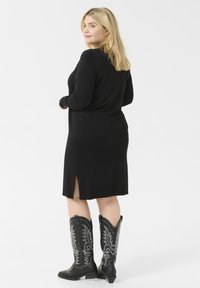 Svart långärmad klänning med sidoflikar, tillverkad av mjukt material, kombinerad med svarta cowboystövlar med silverbroderi.
