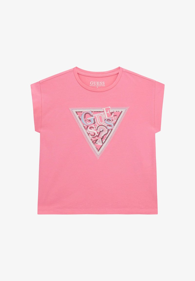 Růžové triko s krátkým rukávem vyrobené z organické bavlny, které obsahuje grafiku trojúhelníku se slovem "GUESS" v stříbrné barvě a různými texturami.
