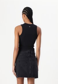 Svart ermeløs topp med ribbet tekstur og rund hals, kombinert med svart denimskjørt med baklommer og rett snitt.