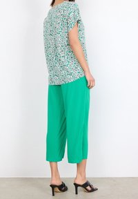 Blomsterprint top i hvid, grøn og blå, parret med ensfarvede grønne cropped bukser. Sorte hælede sandaler fuldender outfittet.
