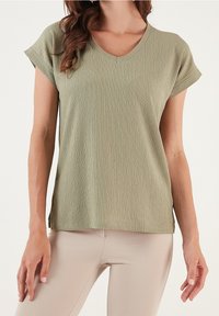 Maglietta corta a maniche corte di un verde chiaro, con un collo a V, caratterizzata da un fit rilassato e un tessuto morbido e traspirante.