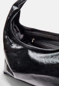 Črna usnjena torbica z sijočim zaključkom, prostornim notranjim delom in žepom z zadrgo. Mehka struktura in ukrivljena ročaj za enostavno nošenje.