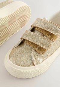 Baskets dorées brillantes avec deux bandes Velcro, bout arrondi et semelle en caoutchouc blanc texturé présentant un motif en zigzag.