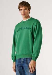 Sweat-shirt en coton vert avec col rond, poignets et ourlet côtelés, portant l'inscription "PEPE JEANS" imprimée en arc de cercle sur la poitrine.
