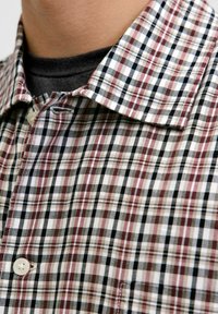 Camicia a maniche lunghe a quadri nei colori bianco, nero e bordeaux. Presenta un colletto alla francese e una tasca sul petto, realizzata in un tessuto morbido e testurizzato.