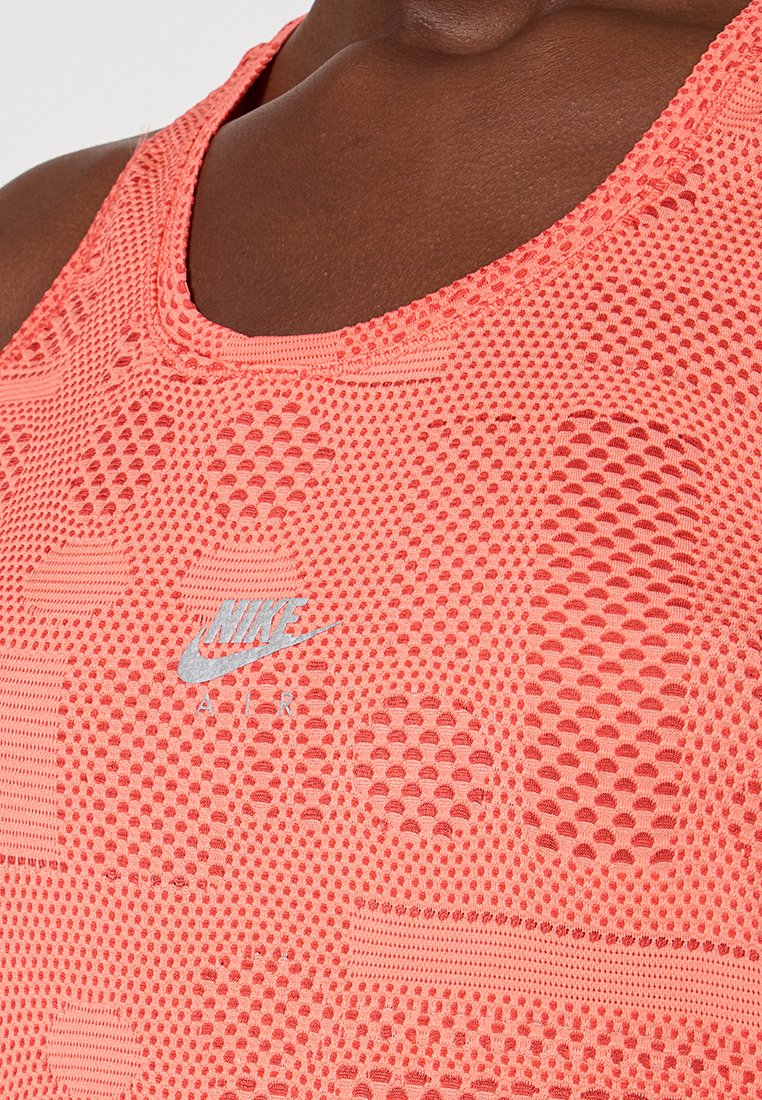 Korallenfarbenes Sport-Top aus Mesh mit einem strukturierten Design, das kreisförmige und rechteckige Muster aufweist. Mit silbernem Nike-Logo auf der Vorderseite.