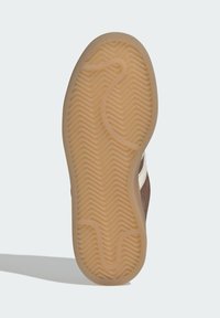 Brown sneaker sole with a herringbone pattern. Light tan rubber material with a smooth texture. Features a curved groove design and subtle detailing.