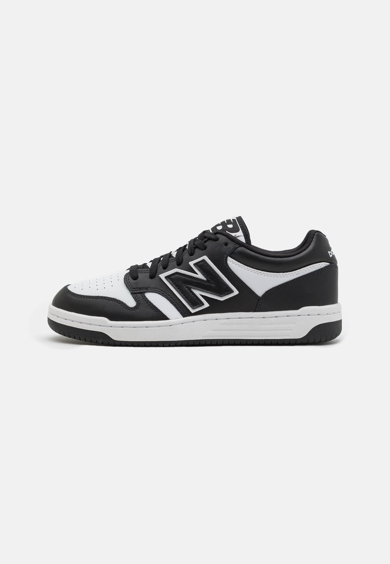 Baskets basses noir et blanc avec logo "N" sur le côté, fermeture à lacets et semelle en caoutchouc sur un fond uni.