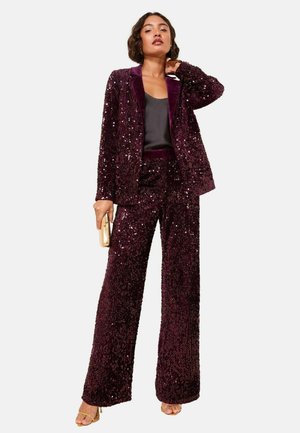 Sequin-embellished suit in deep purple with a fitted blazer and wide-leg pants. Features a contrasting dark satin inner collar. Gold clutch accessory.