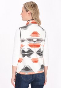 Gilet in pile bianco con motivi geometrici arancioni e grigi, design senza maniche, colletto alto e texture morbida. Indossato sopra una camicia a maniche lunghe.