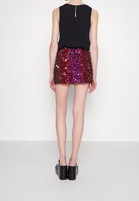 Top senza maniche nero abbinato a una gonna corta e aderente di paillettes che sfuma dal rosso scuro al viola. La modella indossa scarpe con zeppa nere.