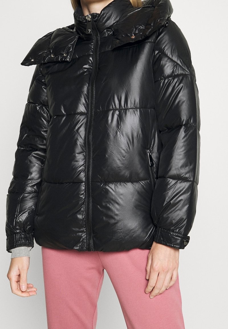 Černá prošívaná bunda s lesklým povrchem, vysokým límcem, zipovým zapínáním a knoflíkovými detaily na oversized límci a manžetách.