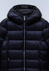 Granatowa kurtka puchowa z odczepianym kapturem, z pikowanym wzorem, srebrnym zamkiem błyskawicznym i bocznymi kieszeniami. Gładka, błyszcząca tekstura.