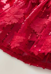Roter, geschichteter Stoff mit Blumenapplikationen, Paillettenverzierungen und einer transparenten Textur, die ein dekoratives und lebhaftes Design schafft.