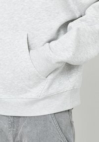 Sweat-shirt gris avec une texture, doté d'une poche kangourou et de poignets côtelés. Le tissu est doux et présente un motif subtil.