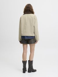 Beige jakke med en brun cordfløyelskrage, sammen med brune suedebukser og knelange svarte støvler, sett fra ryggen.