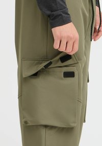 Pantalones cargo verde oliva que cuentan con un gran bolsillo con solapa asegurado con Velcro y una cintura con cordón. Tela suave con un ajuste estructurado.