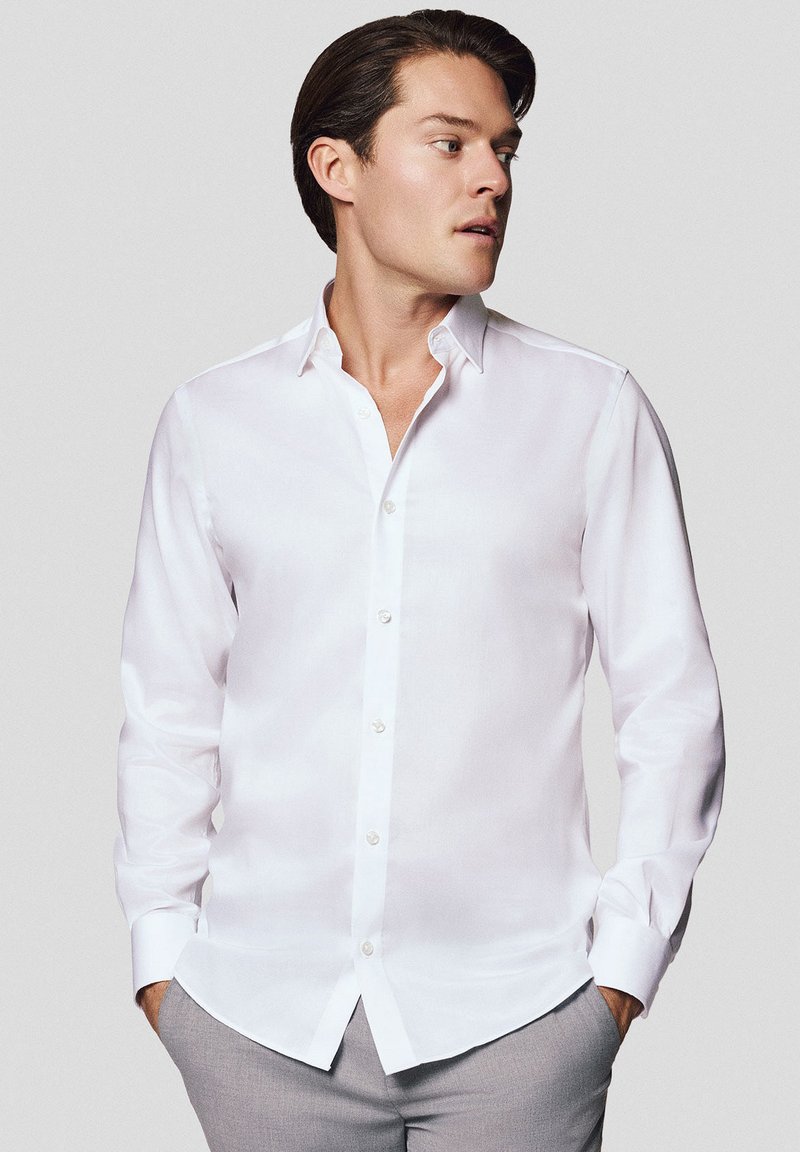 Biała koszula z guzikiem, wykonana z gładkiego materiału, z klasycznym kołnierzykiem i długimi rękawami, o dopasowanym kroju i subtelny połysku.
