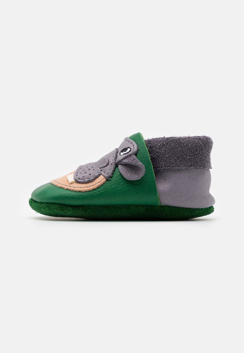 Chausson doux vert et gris pour tout-petit avec un visage d'animal, des oreilles et un revers de cheville duveteux, montré de profil sur fond blanc.