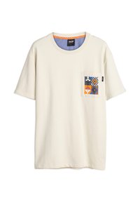 T-shirt en coton beige clair à manches courtes, encolure ronde, avec un détail de poche géométrique coloré présentant des motifs bleus, orange et noirs.