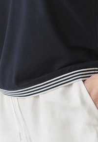 Navy lyhythihainen paita, jossa on raidallinen ribbireuna, valmistettu pehmeästä kankaasta, yhdistettynä vaaleisiin naruhousuihin.
