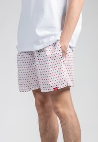 Hvite shorts med rødt hjerte mønster, sidelommer og et lite rødt merke. Laget av lettvevd stoff, med en avslappet passform.