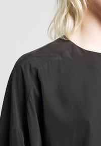 Svart, lättvikts långärmad topp med en slät yta, som har en bred halsringning och raglanärmar. Minimalistisk design, inga synliga knäppningar.