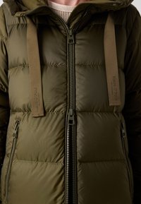 Chaqueta acolchada verde con cierre delantero, grandes secciones acolchadas, correas contrastantes en color beige y bolsillos laterales con cremallera. Cuenta con un cuello alto.