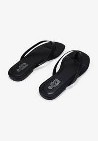 Chanclas negras con tiras finas, plantilla texturizada y suela plana. Logotipo impreso en la plantilla. Diseño minimalista y acabado suave.