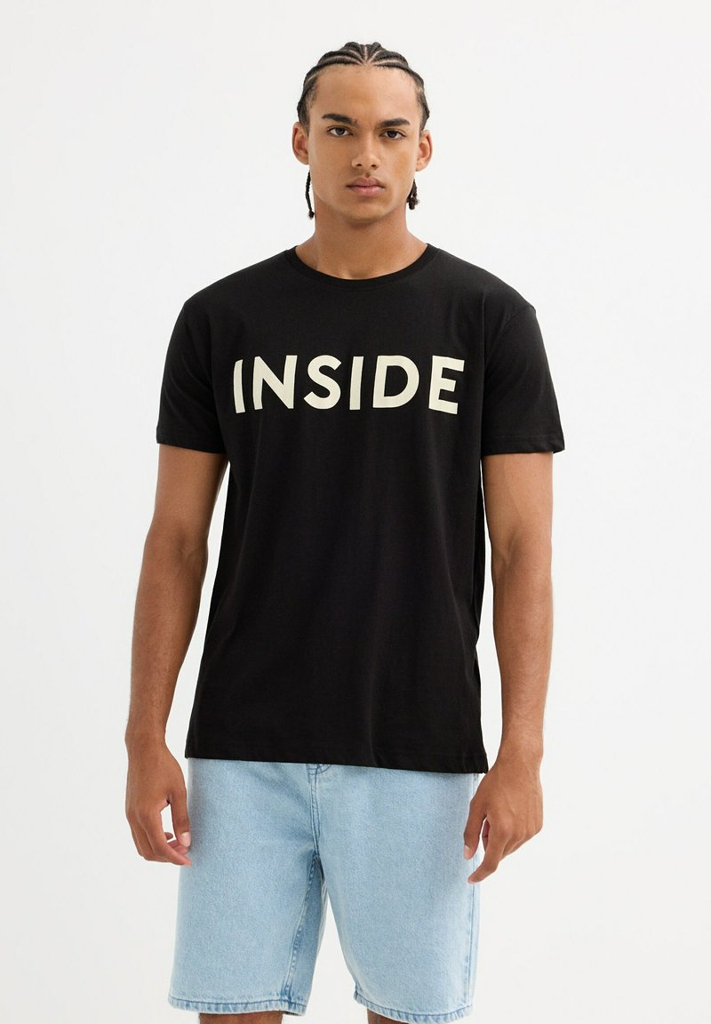 Camiseta de manga corta negra con gran texto "INSIDE" en color crema. Presenta un corte relajado, fabricada en suave material de algodón.