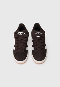 Ténis de camurça castanha com riscas brancas, biqueira arredondada e atacadores planos. Apresenta um logótipo circular na língua e sola de borracha.