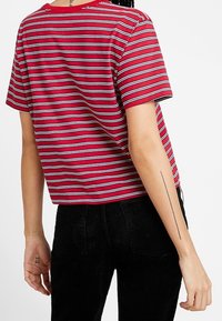 Röd och vitrandig t-shirt med kort ärm och löst snitt, i kombination med svarta kordbyxor. Halsringningen är ribbad och av crew stil.