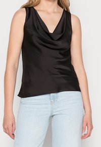 Top senza maniche in satin nero con scollatura a drappeggio, texture liscia e vestibilità rilassata, abbinato a jeans azzurri chiari.