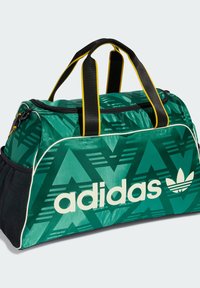 Zöld sporttáska sárga díszítéssel, mintás anyagból, fekete hálós oldalzsebbel és fehér "adidas" logóval az elején.