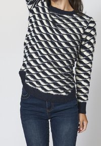Pletený svetr s námořnickými a bílými spirálovými pruhy, texturovanou tkaninou, kulatým výstřihem a žebrovanými manžetami a lemem. Nosený s tmavými džíny.