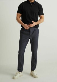 Czarna koszulka polo z krótkim rękawem, granatowe spodnie i białe trampki. Polo ma kołnierzyk i trzy guziki; spodnie mają teksturowane wykończenie.