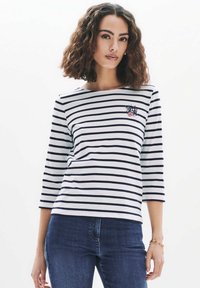 T-shirt med trekvart ärm i vit och marinblå randig design, med en blomsterbroderad patch på vänster bröst, tillverkad av mjukt och stretchigt material.