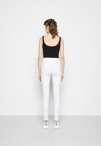 Body preto sem mangas combinado com calças brancas ajustadas, apresentando uma textura suave, design minimalista e ténis brancos.