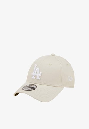 Adjustable beige baseball cap features a white embroidered "LA" logo on the front, with a curved brim and six ventilation eyelets.