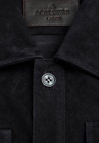 Sort ruskindsjakke med krave, frontknaplukning med logoknap og syningsdetaljer langs kanterne.