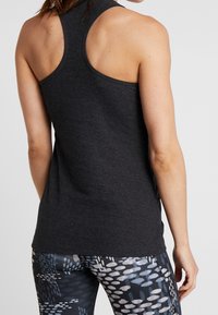 Musta ribbiä tanktoppi, jossa on racerback-muotoilu. Kankaassa on pintakuvioitu viimeistely. Yhdistetty kuviollisiin, istuviin legginsseihin, joissa on abstrakti muotoilu.