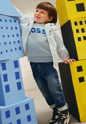 Giacca blu a strisce con zip, felpa azzurra chiara con logo "BOSS", jeans in denim scuro e sneakers nere con dettagli bianchi e arancioni.