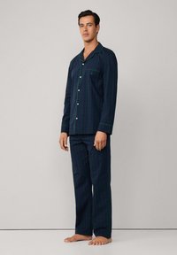 Conjunto de pijama de algodón a rayas en azul marino y verde, con una camisa abotonada que presenta un bolsillo y un cuello en contraste, acompañada de pantalones rectos.