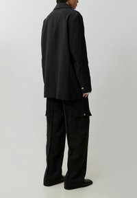 Zwarte lange blazer met een rechte snit en twee knopen, gecombineerd met cargo pantalons met een relaxte pasvorm, zijzakken en een gladde afwerking.