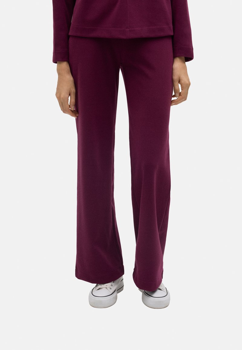 Pantalones acampanados color burdeos, hechos de una tela suave, con una textura lisa y un corte relajado. Combinados con zapatillas blancas de estilo casual.