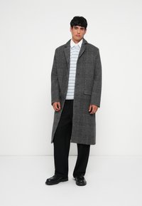 Gray plaid long coat with a notched collar, worn over a light striped shirt and black trousers. Black shoes complete the ensemble.