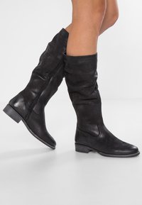Bottes en cuir noires montant jusqu'au genou avec un design décontracté, un talon bloc bas, une fermeture éclair latérale et une texture lisse.