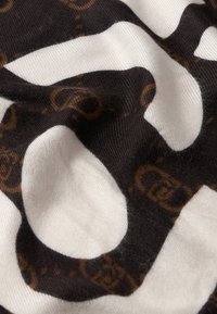 Primo piano di un tessuto bianco e nero con un motivo a maglie di catena marroni stampato su una stoffa morbida e leggermente spiegazzata.